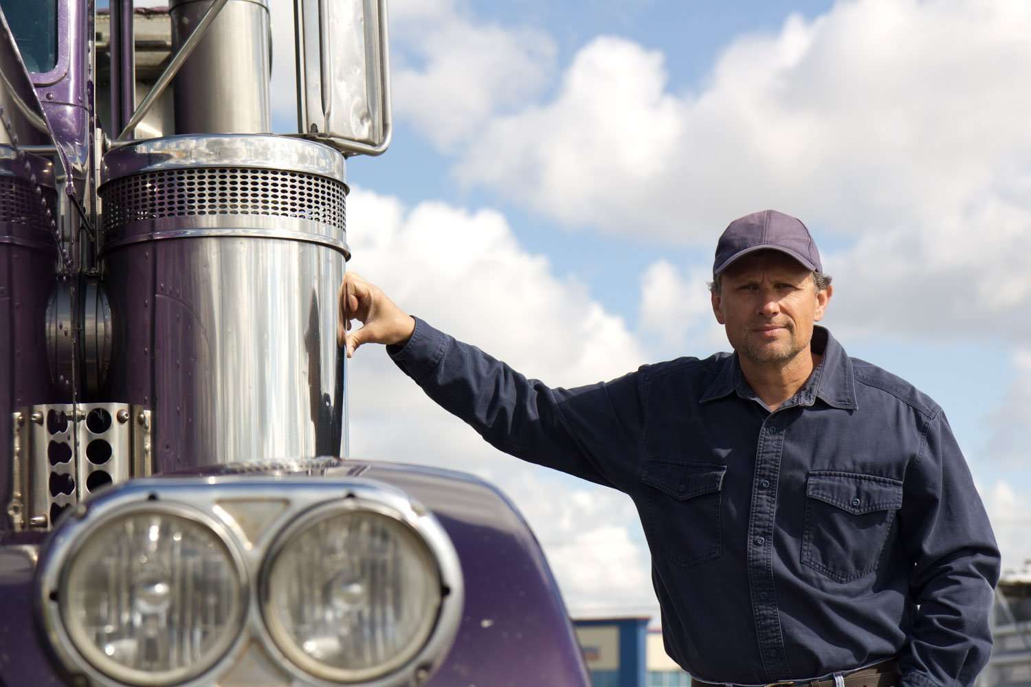 A man standing next to his semi-truck, which is equipped with a portable truck toilet.