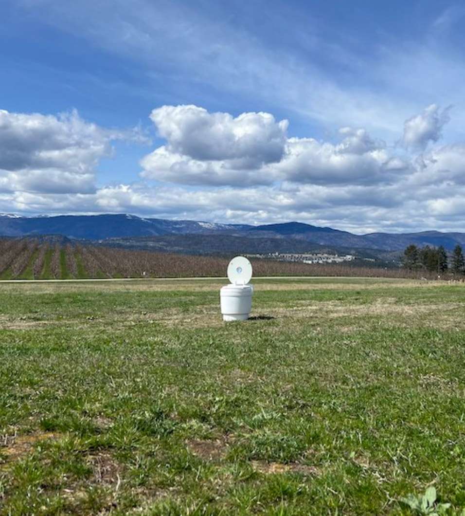 Portable RV toilet sitting in the middle of a large grass field.